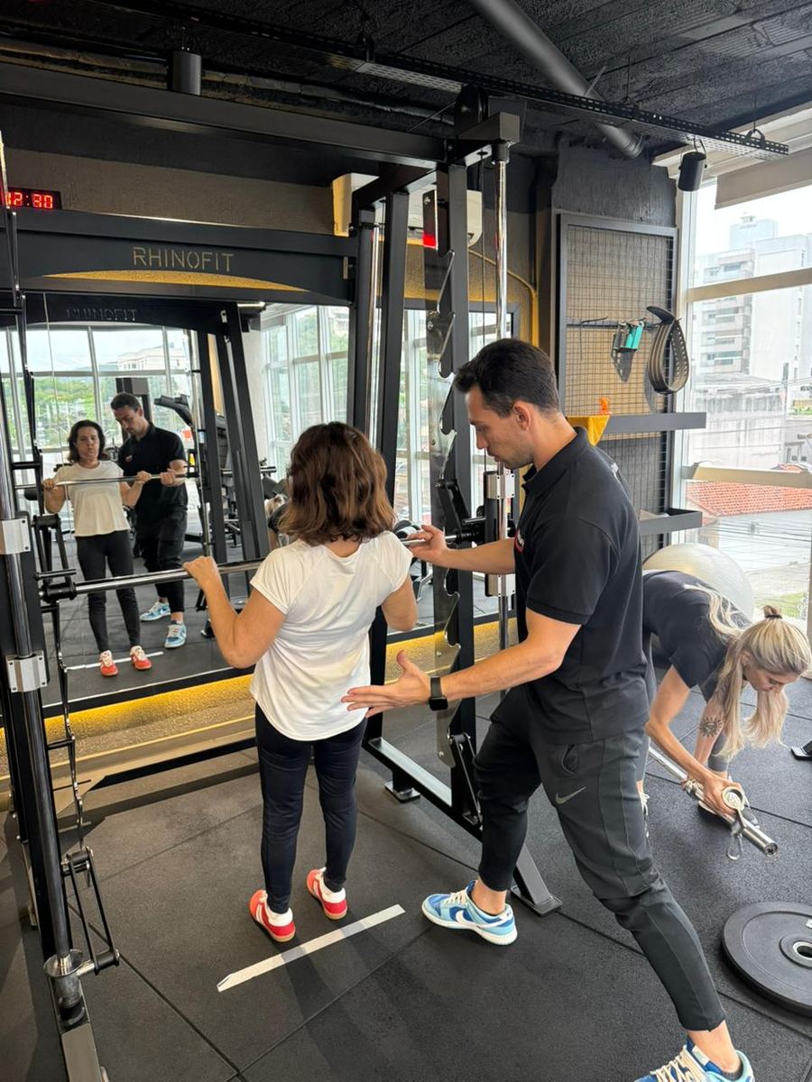Professor acompanhando aluna no smith machine